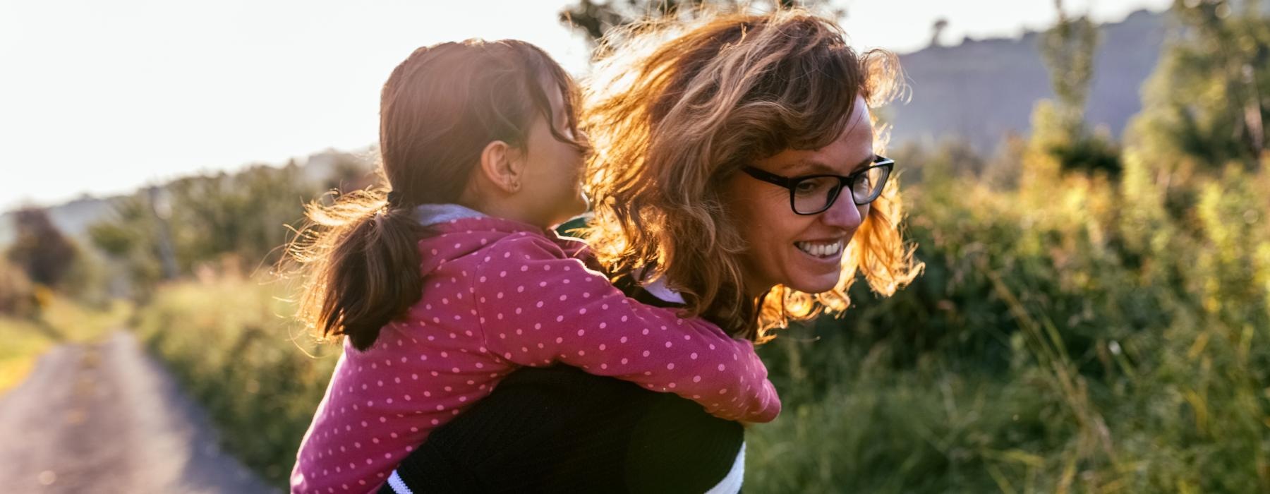 mother piggy backing her daughter on a dirt trail